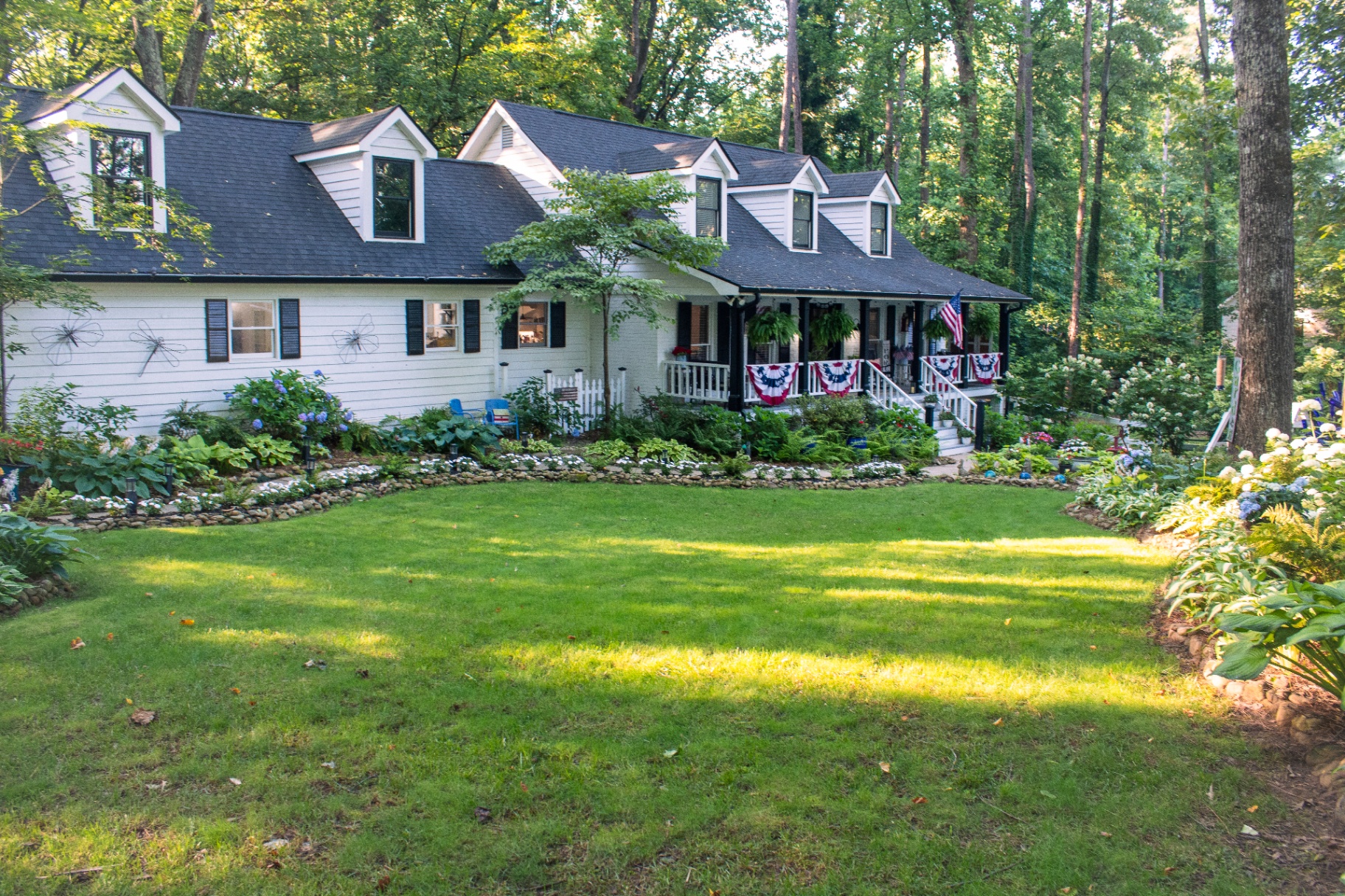 White farmhouse with wraparound porch surrounded by lush hydrangea and hosta gardens in Acworth, Georgia